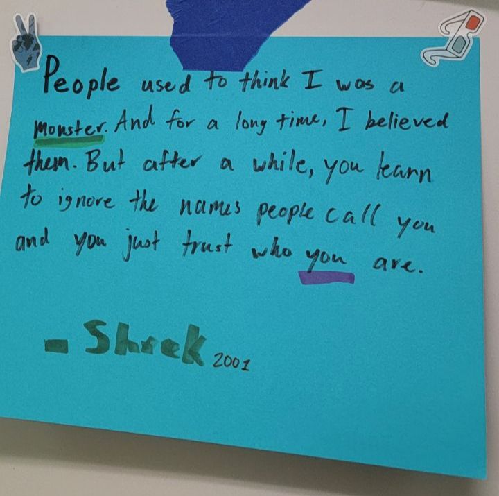 Handwritten quote on a blue sticky note mentioning overcoming negative labels, attributed to Shrek, 2001.