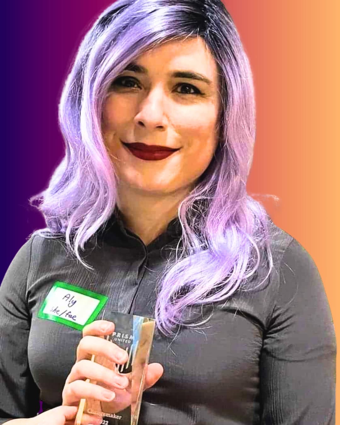 AlysandriaEmbergale Person with long lavender hair, wearing a gray shirt and name tag, holding a clear award against a gradient orange and purple background.