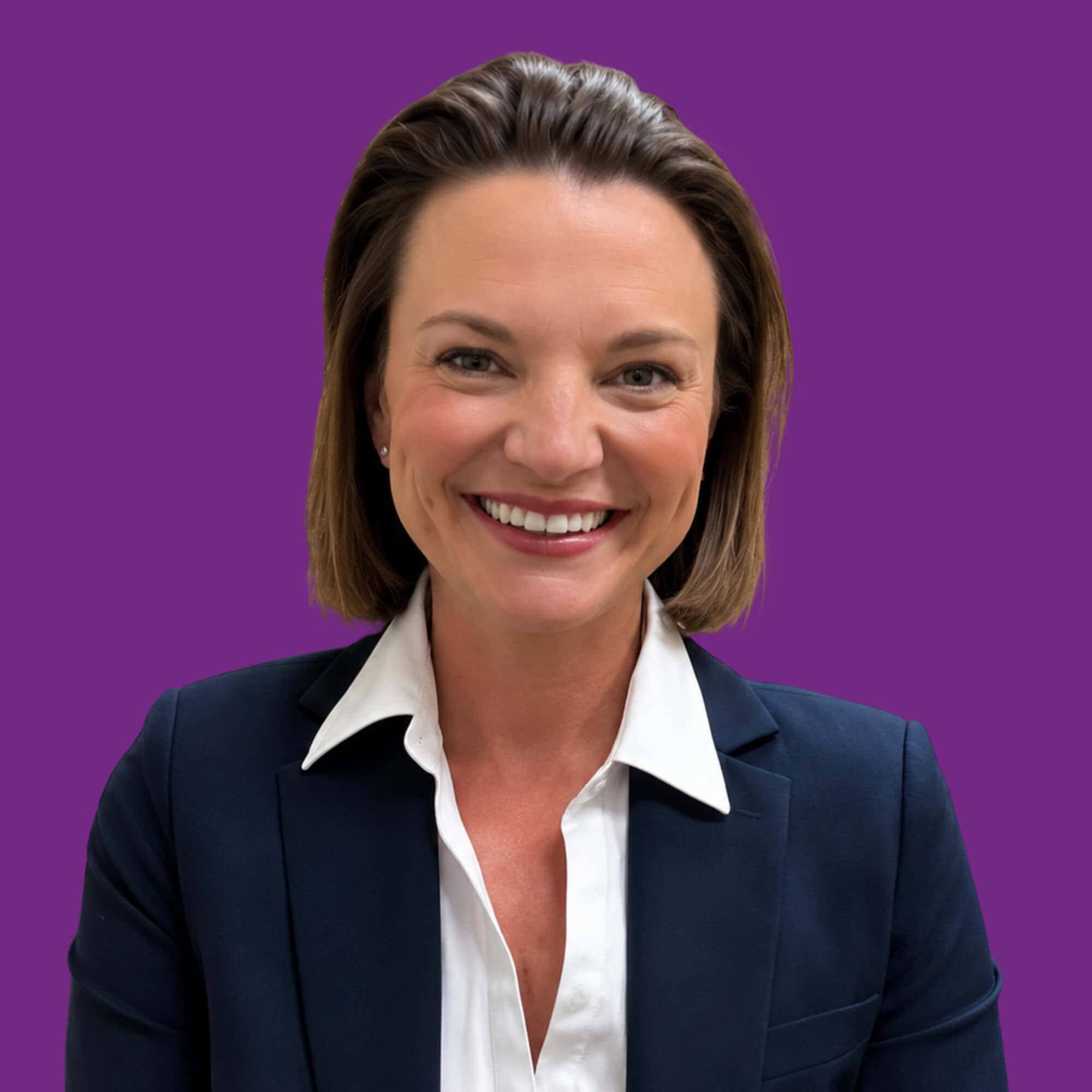Board & Staff Photos Color (9) Smiling woman with short brown hair wearing a navy blazer and white shirt, posed in front of a solid purple background.