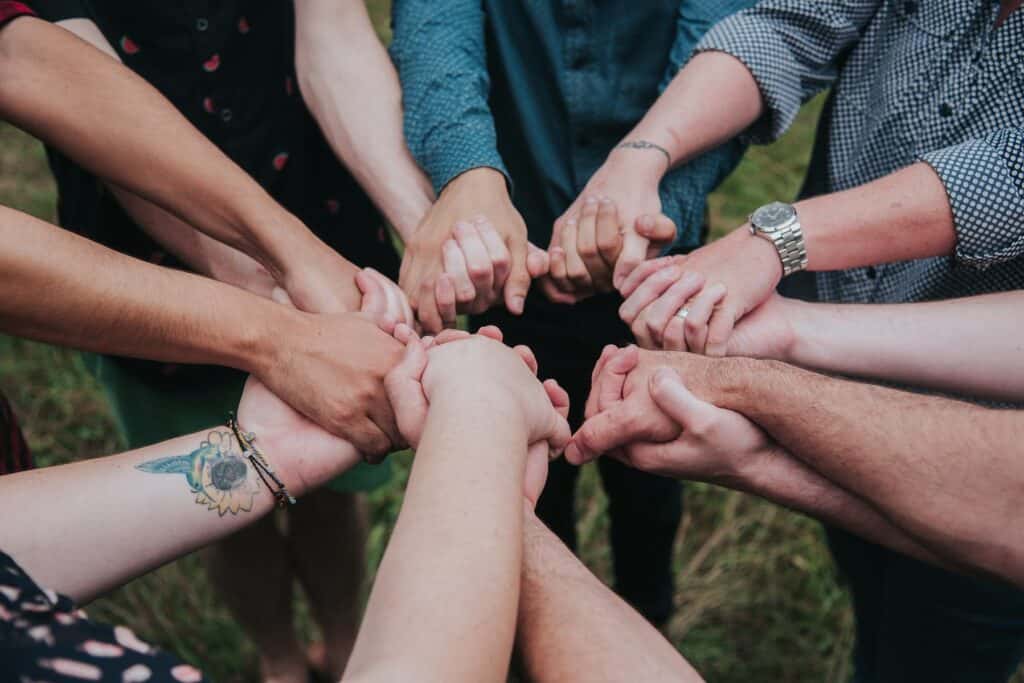 A group of people standing in a circle, their hands clasped together in the center, displaying unity and teamwork.