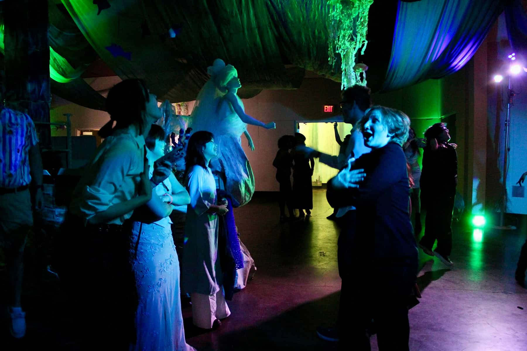 People in costume dancing at a dimly lit Halloween party with colorful lighting and decorations.