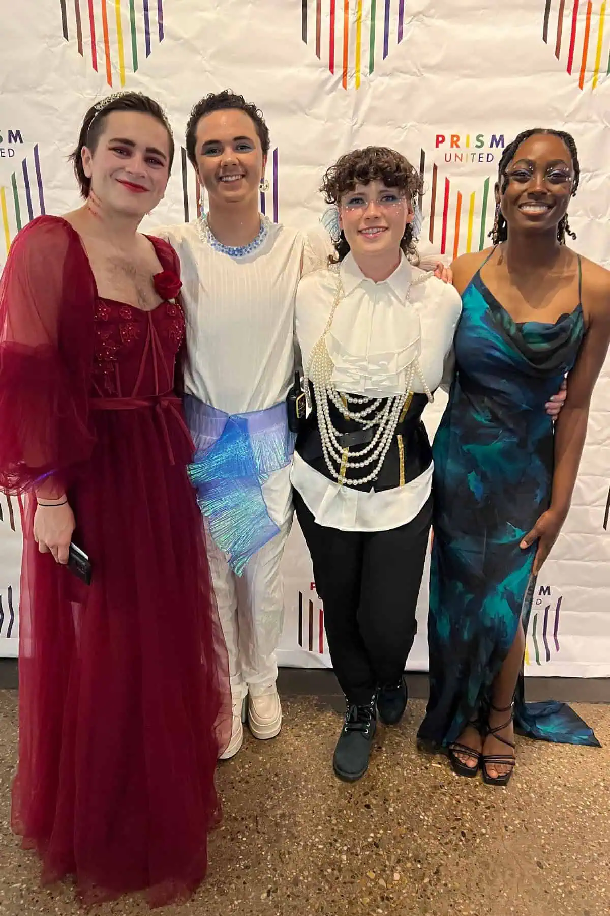 Four individuals in elegant attire posing at an event, each wearing colorful, themed costumes with joyous expressions, standing before a festive backdrop.