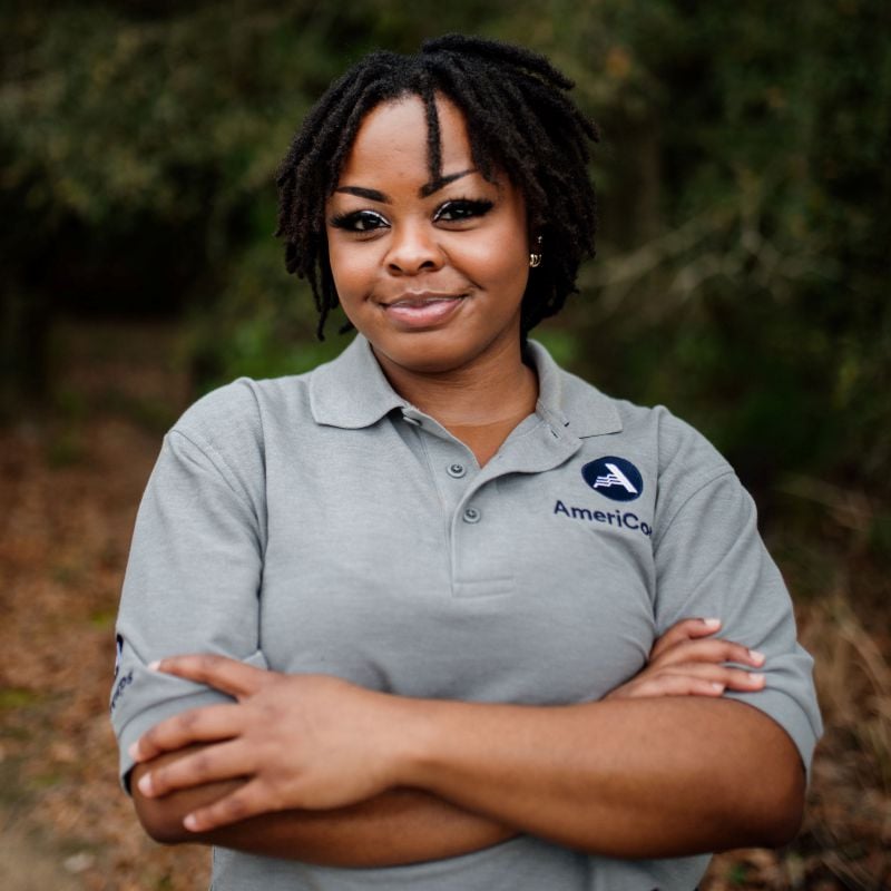 A confident individual with crossed arms wearing a gray shirt with an americorps logo.