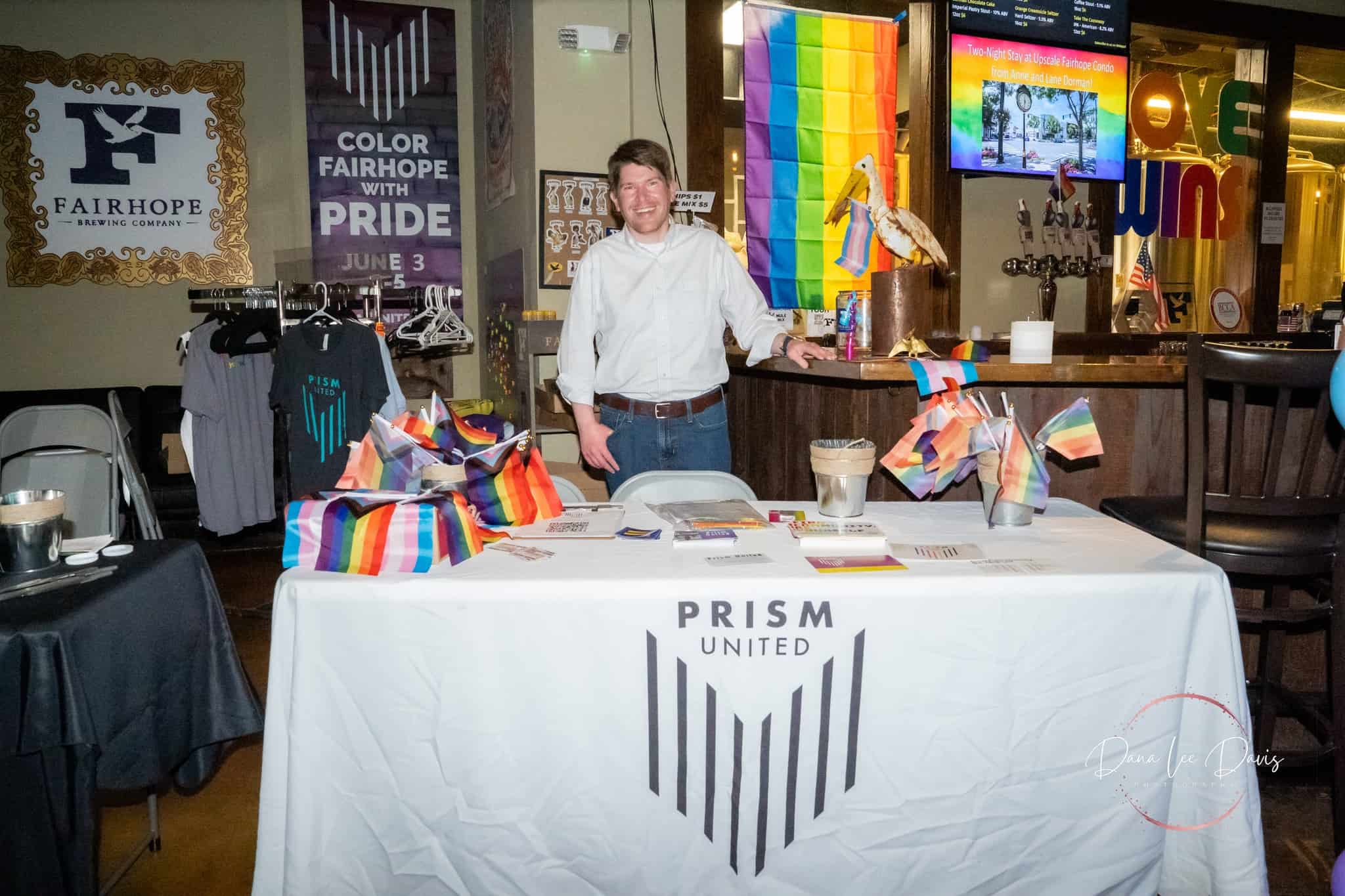 A person standing behind a booth adorned with rainbow flags at an event.
