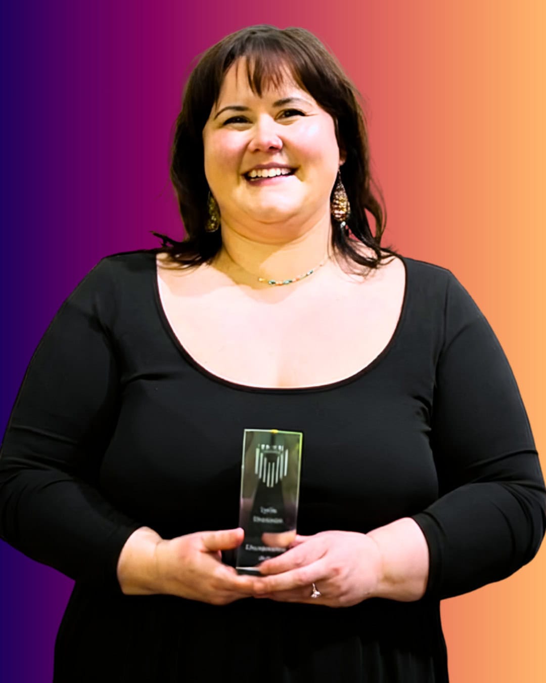 LydiaShantazio A woman in a black dress smiles while holding a glass award against a gradient background.