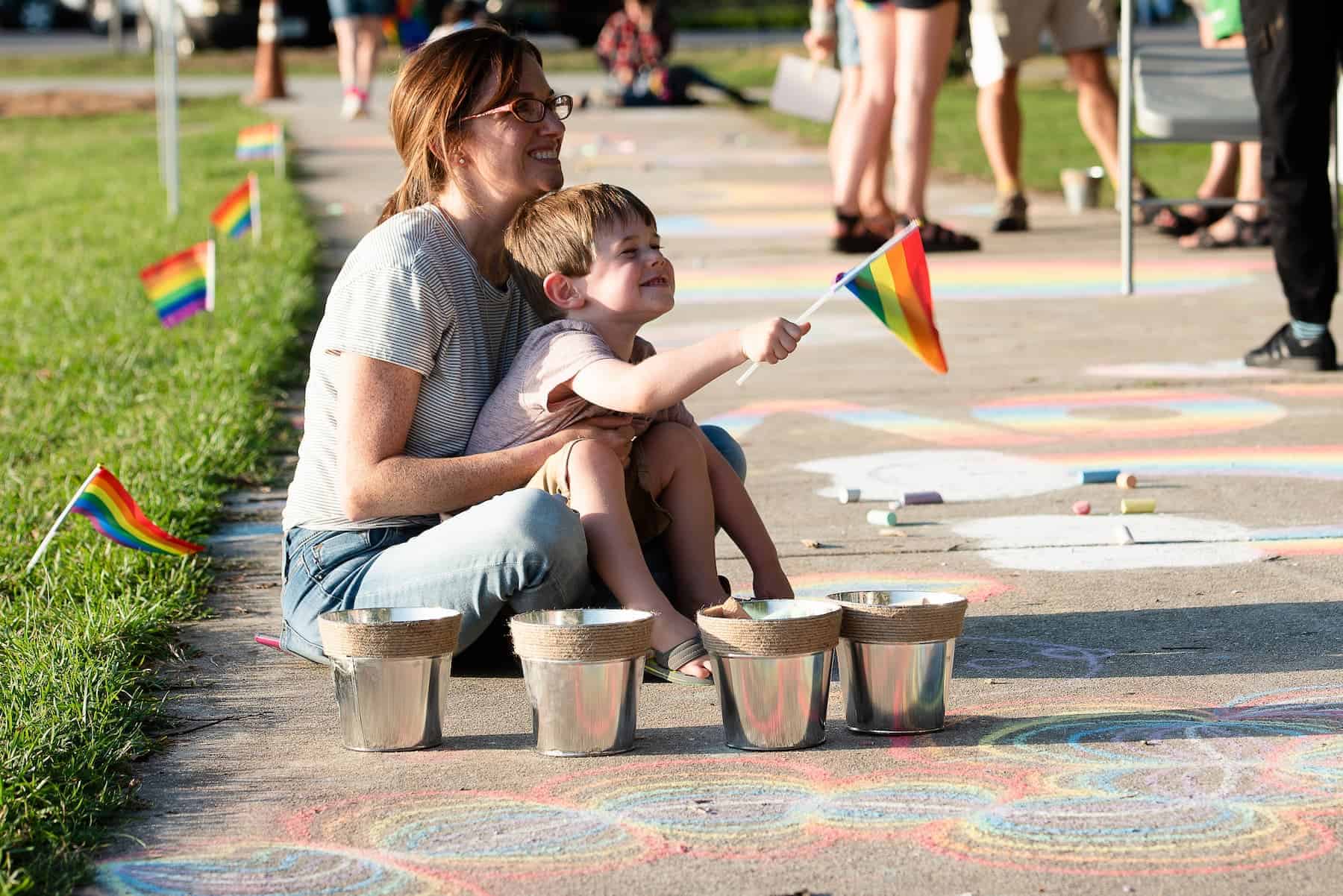 Mother and child sitting with pride flags and sidewalk chalk