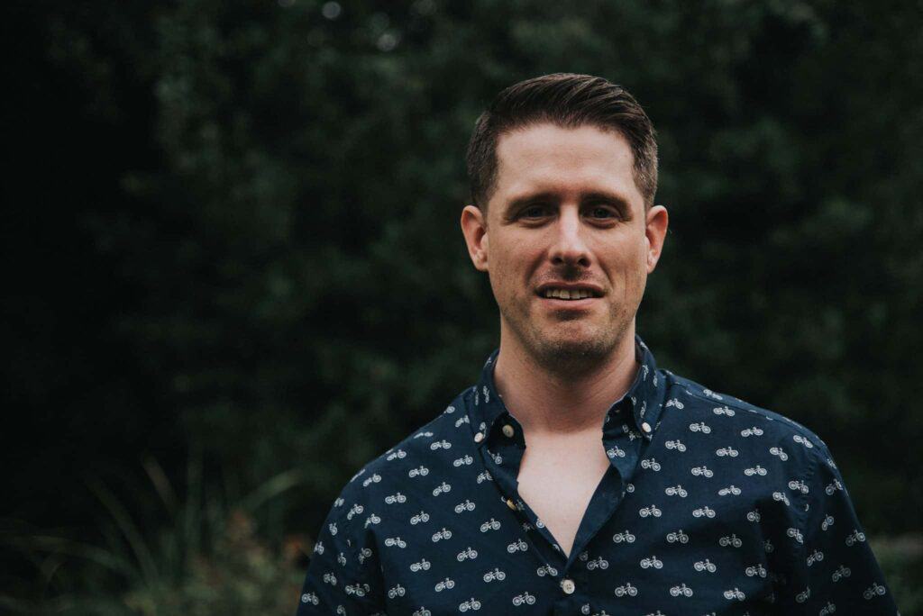 Man in a patterned shirt standing outdoors with a slight smile.