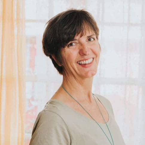 Woman with a short haircut smiling in front of a bright window.
